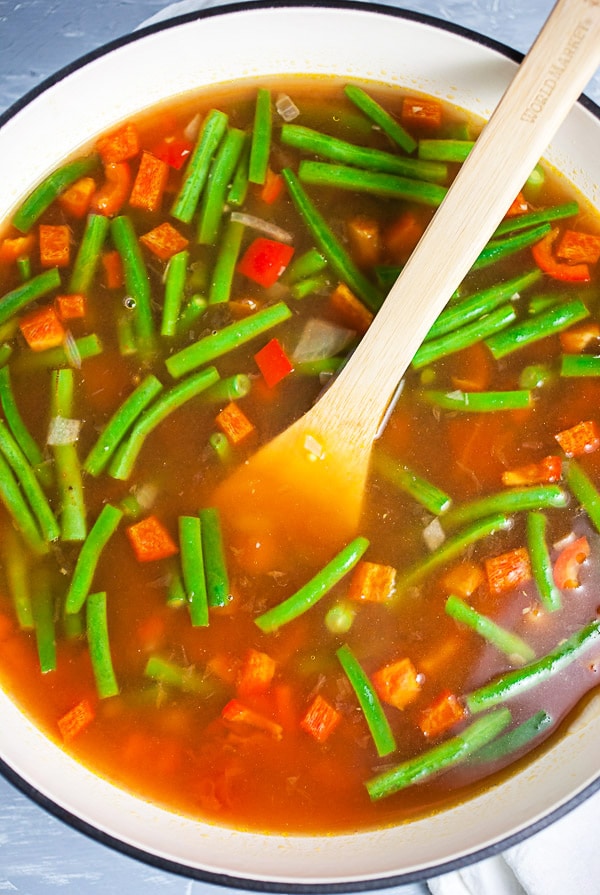 Uncooked vegetable soup in Dutch oven with wooden spoon.