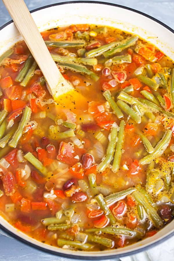 Cooked veggie soup in Dutch oven with wooden spoon.