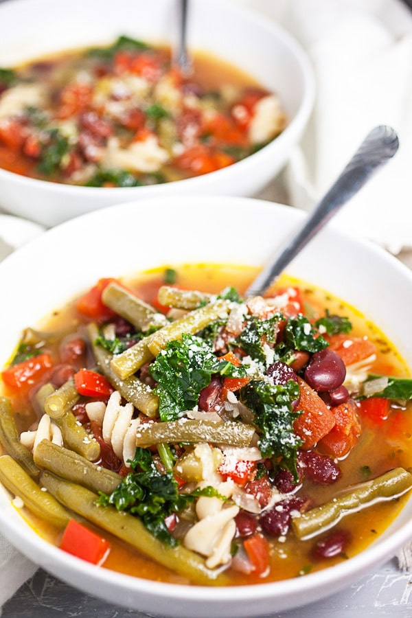 Italian vegetable soup with Parmesan cheese in white bowls with spoons.