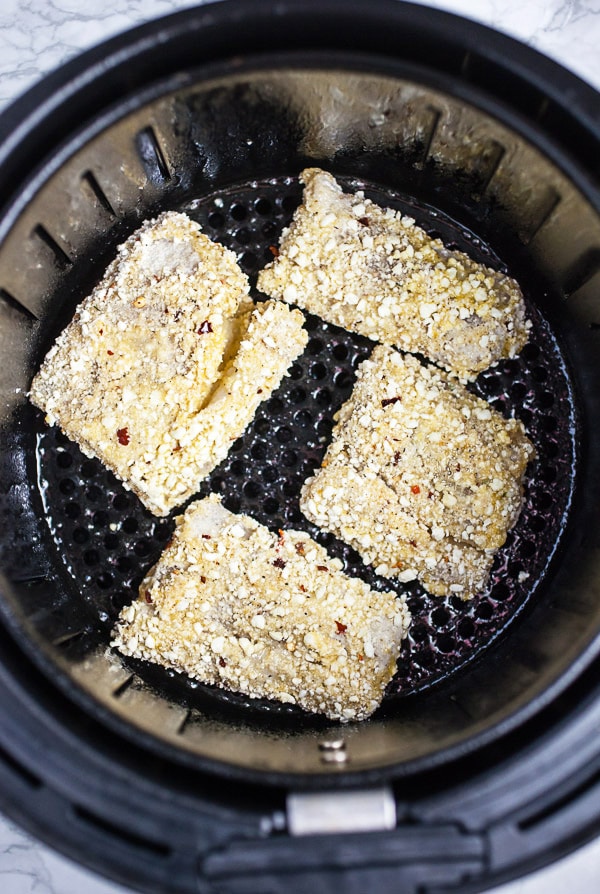 Uncooked breaded fish fillets in air fryer basket.