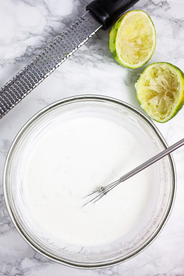 Mexican crema in small glass bowl with whisk, Microplane zester, and limes.