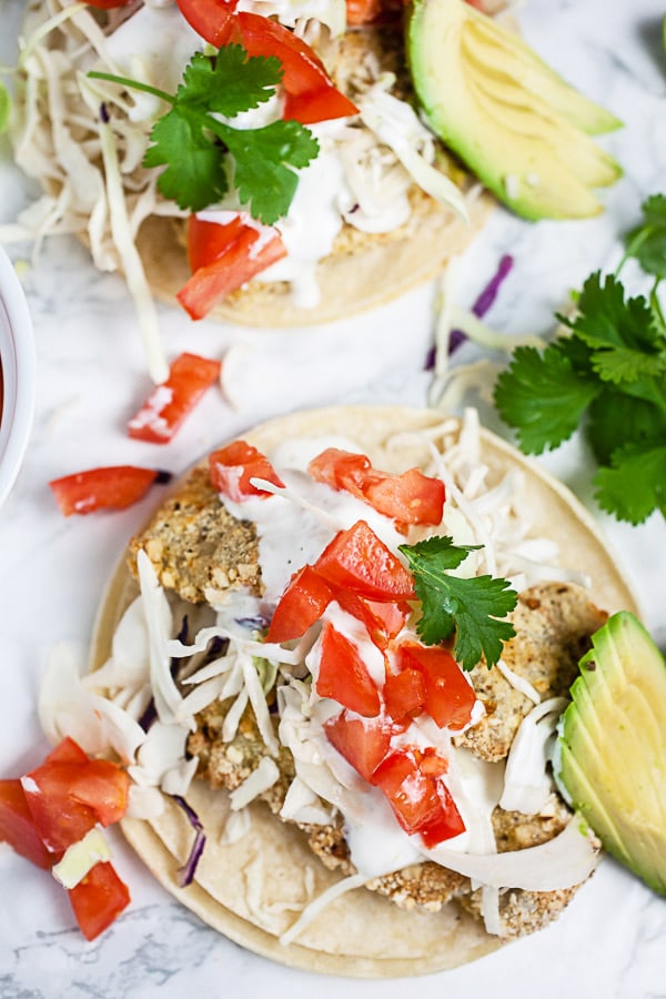Air fried fish tacos on corn tortillas with Mexican crema, cabbage, tomatoes, cilantro, and sliced avocadoes.
