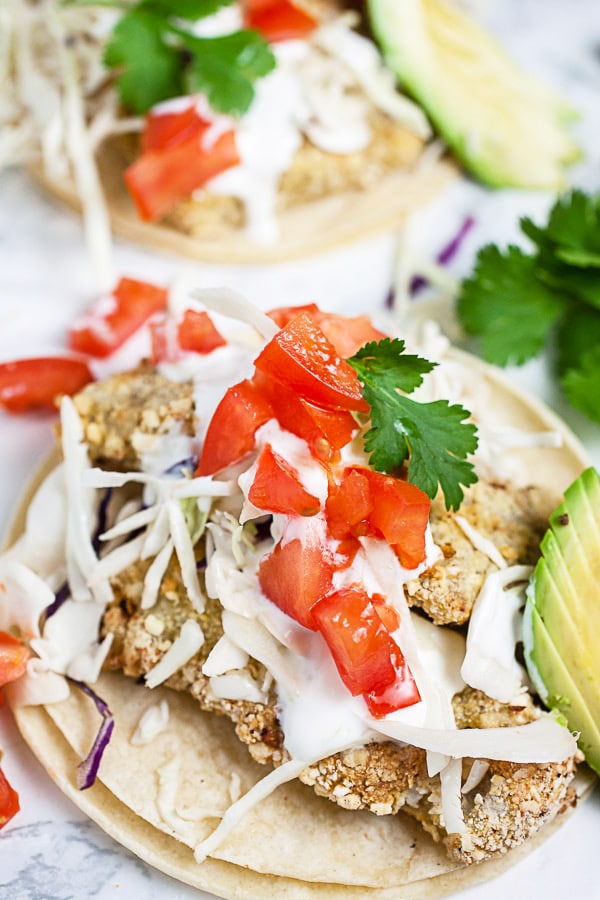 Air fryer fish tacos on corn tortillas with Mexican crema, cabbage, tomatoes, and cilantro.