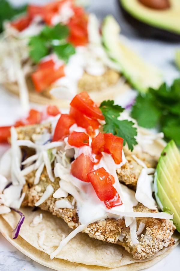 Crispy fish tacos on corn tortillas with Mexican crema, cabbage, tomatoes, cilantro, and sliced avocado.