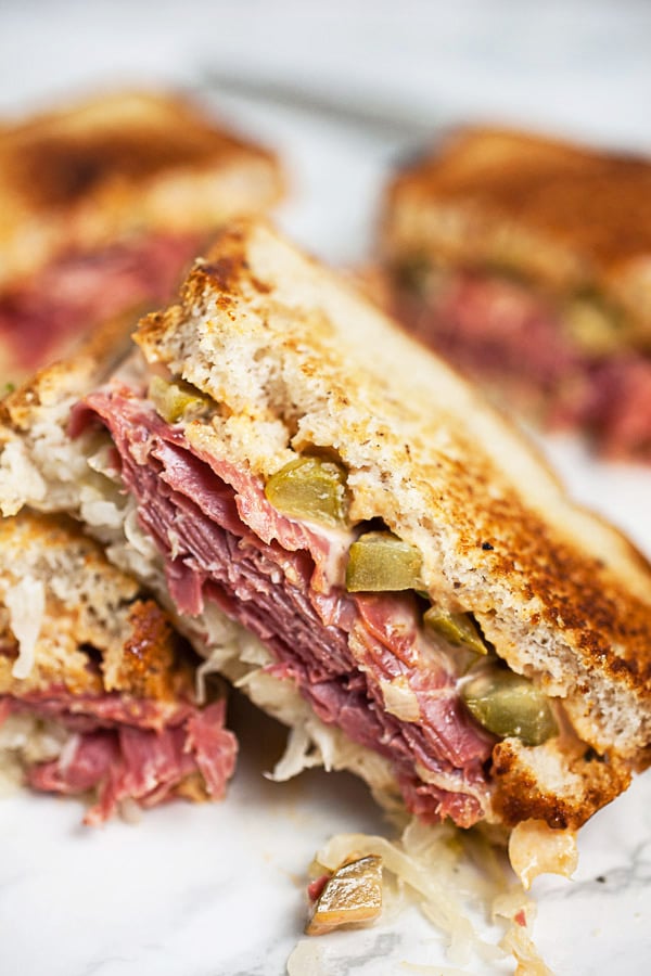 Reuben sandwich with Thousand Island dressing cut in half and stacked on white surface.