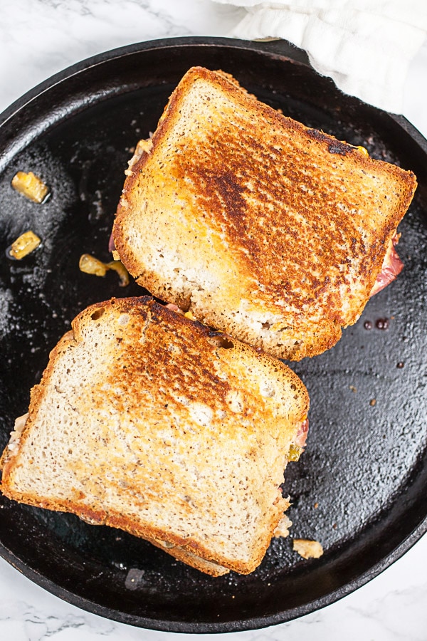 Reuben sandwiches toasting on cast iron griddle.