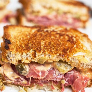 Corned beef Reuben sandwich cut in half on white surface.