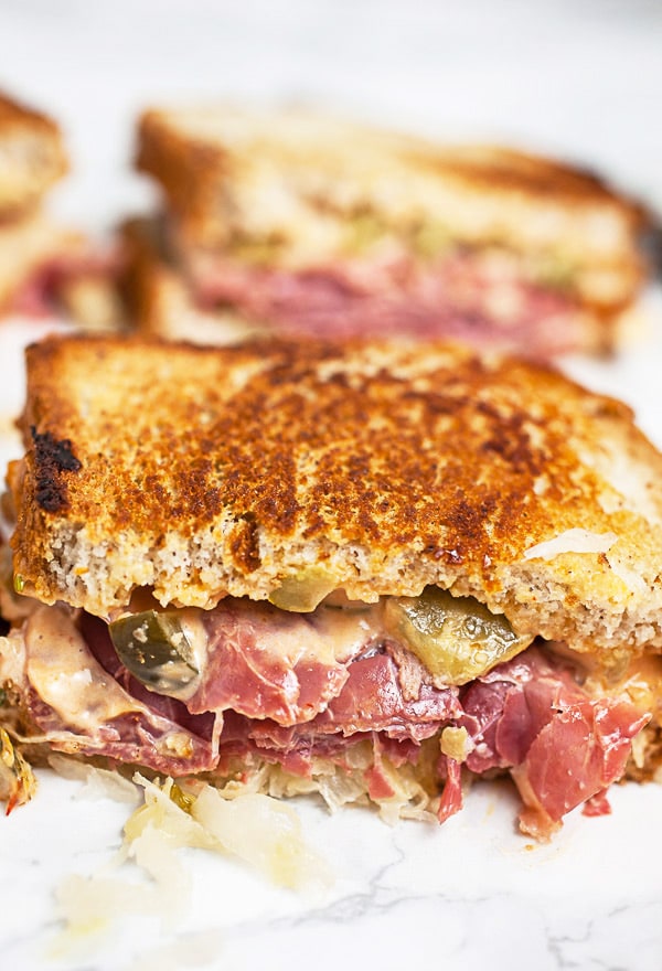 Corned beef Reuben sandwich cut in half on white surface.