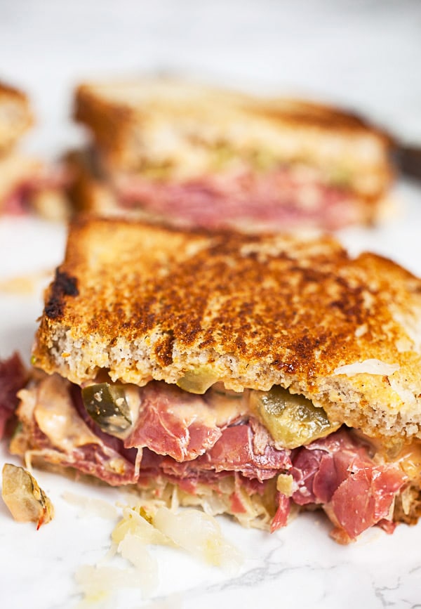 Corned beef Reuben sandwich cut in half on white surface.