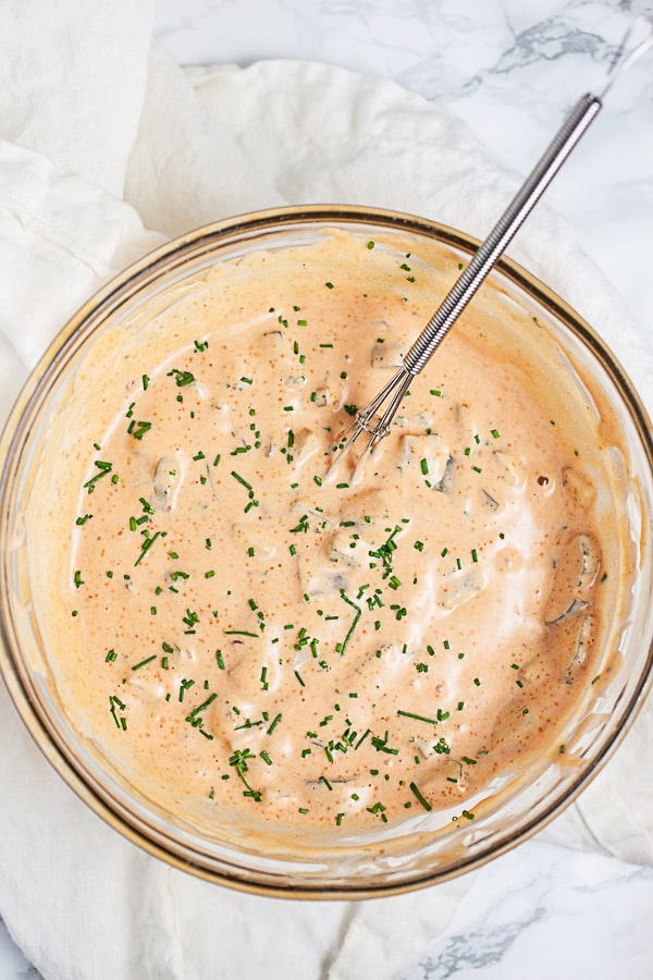 Thousand Island dressing mixed with minced chives in small glass bowl with whisk.