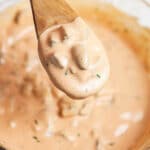 Spoonful of Thousand Island dressing lifted from small glass bowl on wooden spoon.