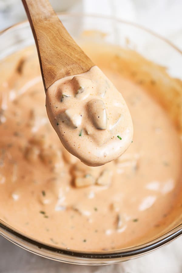 Spoonful of Thousand Island dressing lifted from small glass bowl on wooden spoon.