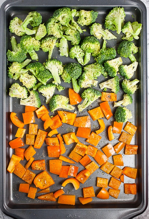 Chopped broccoli and orange bell peppers on metal baking sheet.