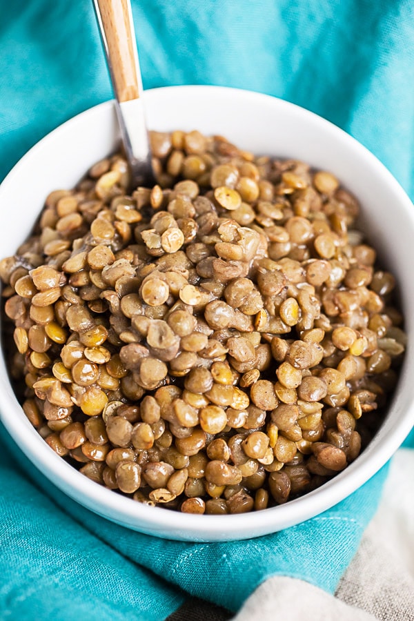 Pressure cooker lentils in small white bowl with fork.