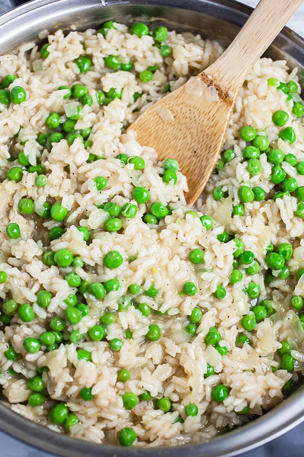 Cooked Arborio rice with peas in skillet with wooden spoon.