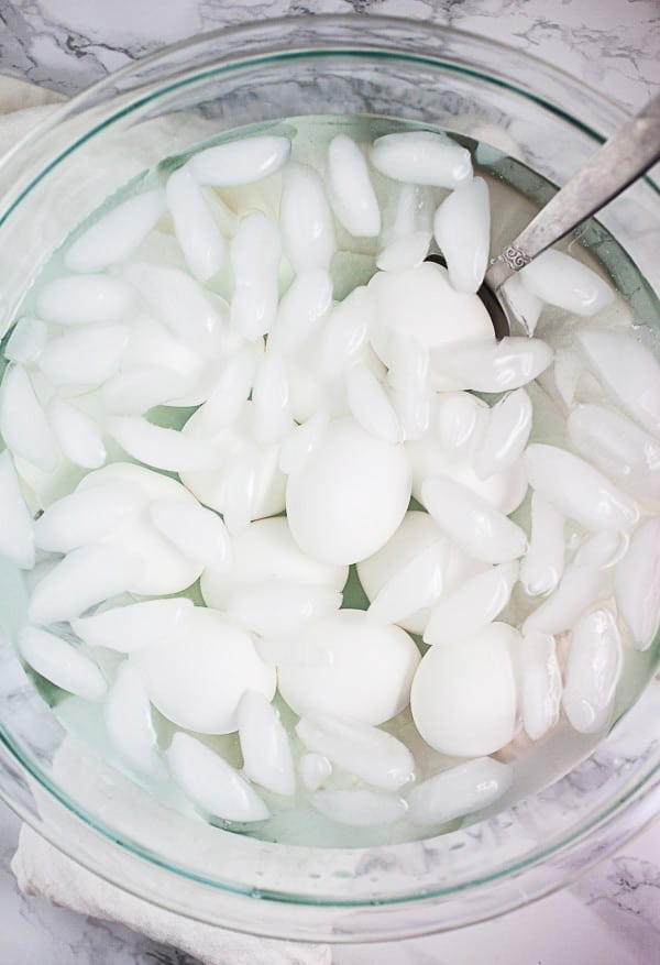 Hard boiled eggs cooling in ice bath in large glass mixing bowl.