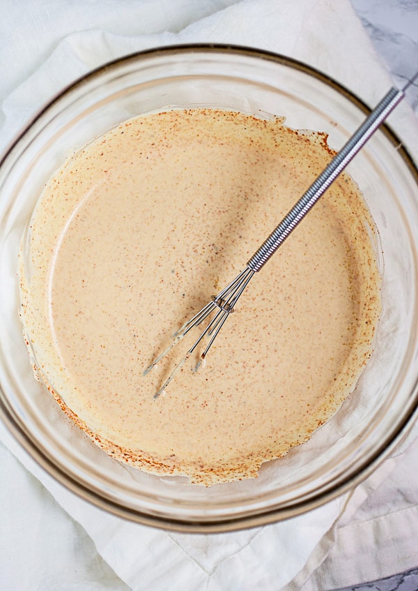 Mayo and mustard dressing in small glass bowl with whisk.