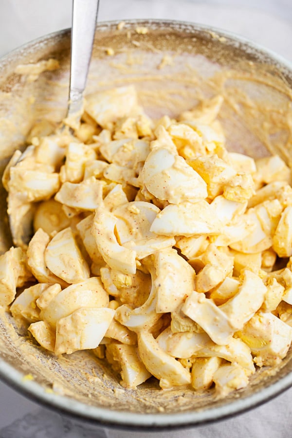 Chopped hard boiled eggs tossed in dressing in ceramic bowl.