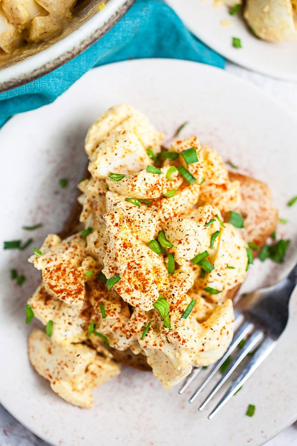 Egg salad on slice of bread on small white plate with fork.