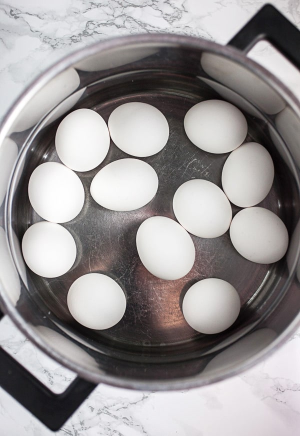White eggs submerged in water in metal pot.