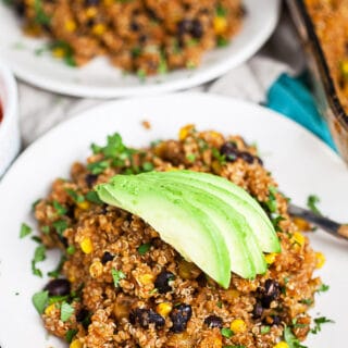 Quinoa enchilada casserole topped with avocado slices on small white plate.