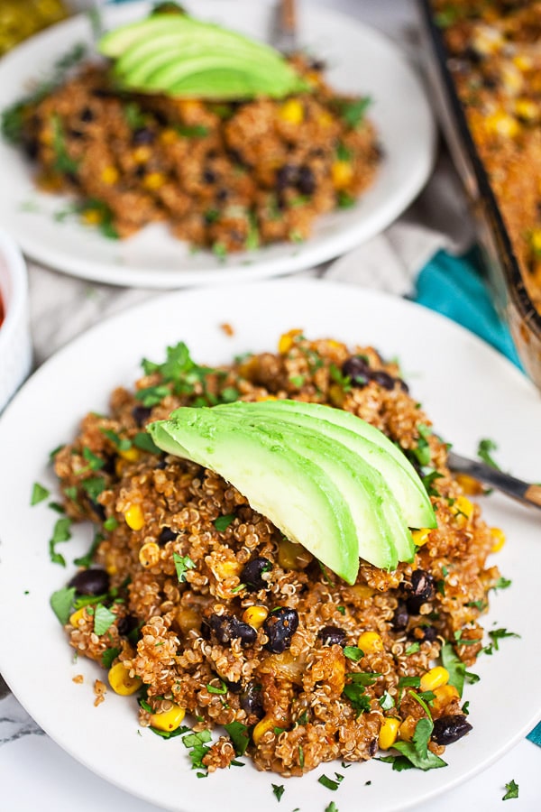 Quinoa enchilada casserole topped with avocado slices on small white plate.