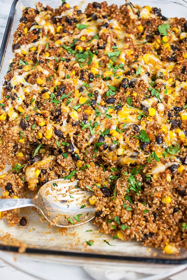 Cooked quinoa casserole in glass baking dish with metal spoon.