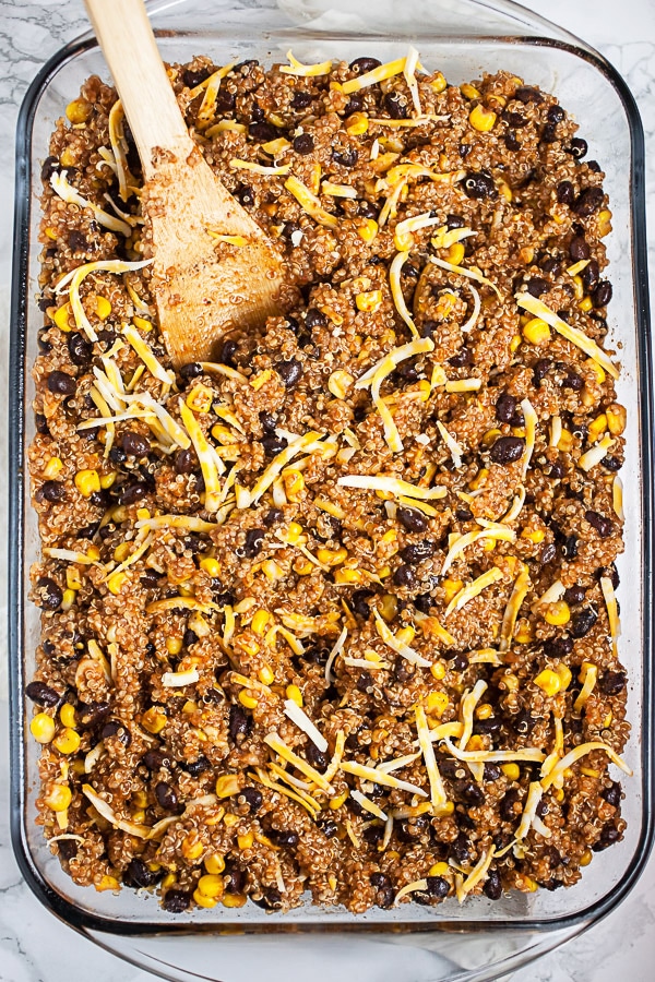 Quinoa, black beans, corn, cheese, and enchilada sauce in glass baking dish.