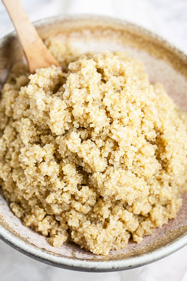 Cooked quinoa in ceramic bowl with wooden spoon.