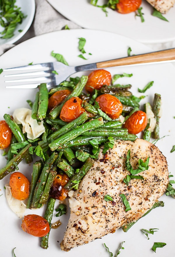 Italian chicken breast, green beans, tomatoes, and Parmesan cheese on white plate garnished with fresh basil.