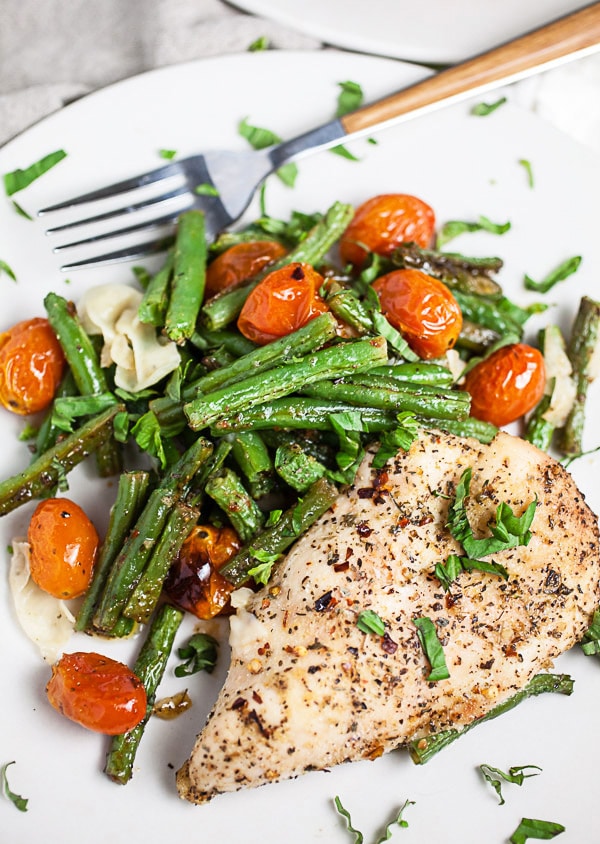 Baked Italian chicken breast, green beans, tomatoes, and Parmesan cheese on white plate with fresh basil.