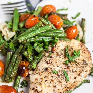 Sheet pan Italian chicken with green beans, tomatoes, and Parmesan cheese on white plate with fork.
