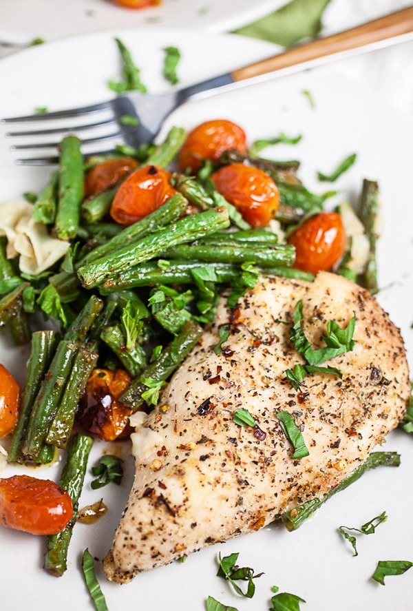 Sheet pan Italian chicken with green beans, tomatoes, and Parmesan cheese on white plate with fork.