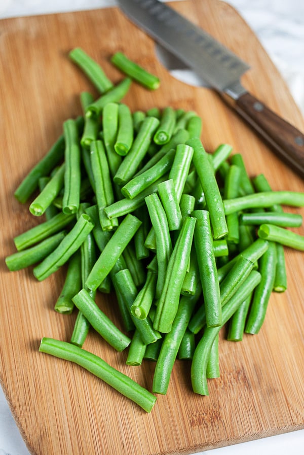 Chopped fresh green beans on wooden cutting board with knife.