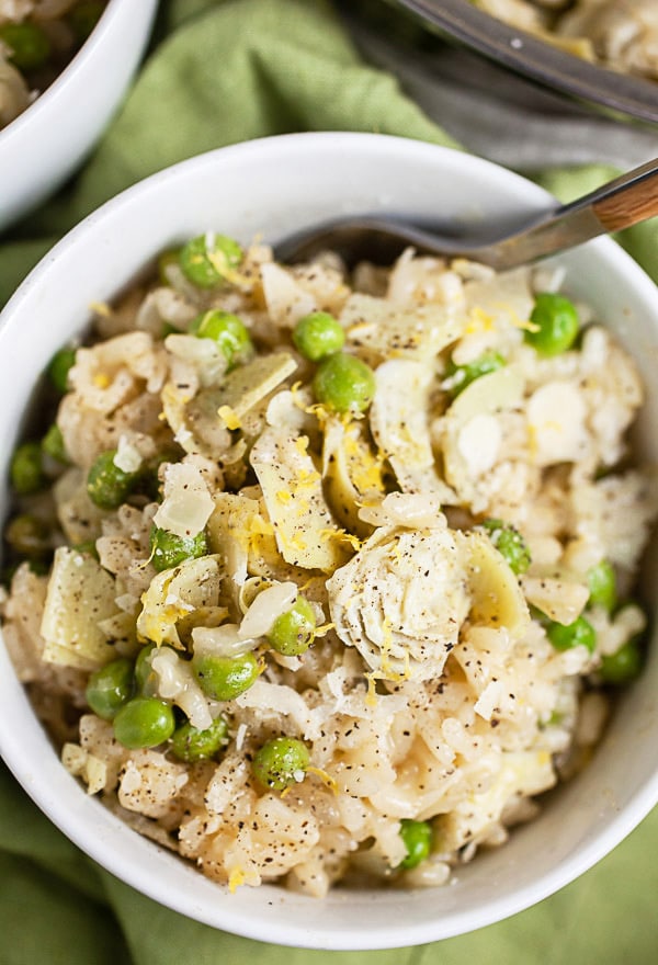 Lemon risotto with peas and artichokes in white bowl with fork.