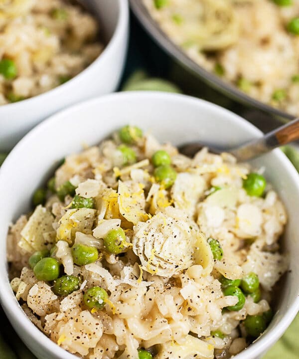 Lemon risotto with peas and artichokes in white bowls.