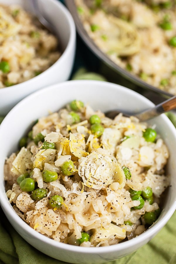 Lemon risotto with peas and artichokes in white bowls.