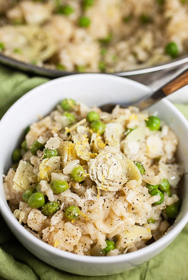 Spring risotto with peas and artichokes in white bowl in front of skillet.