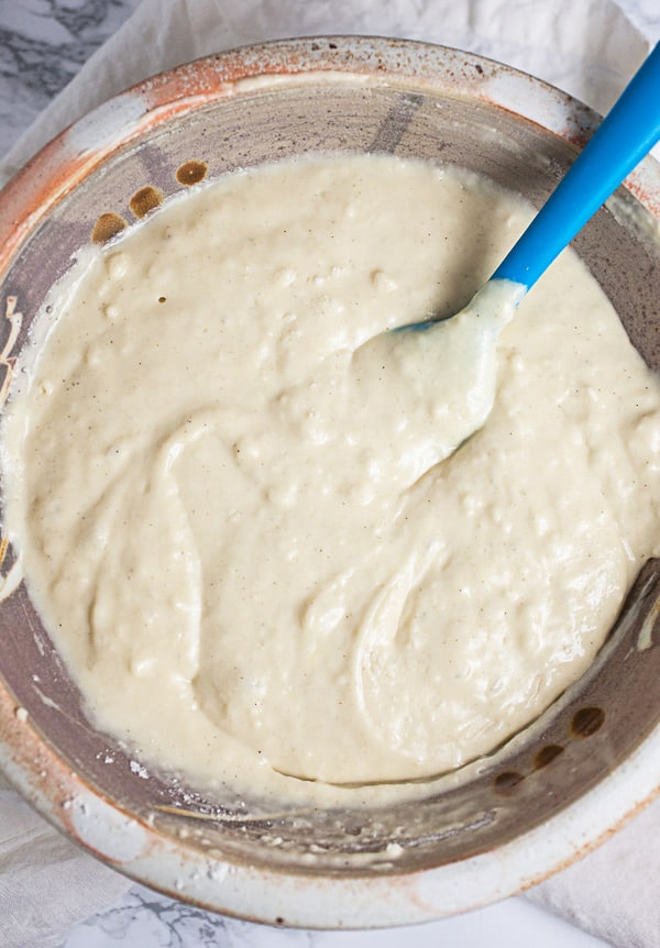 Pancake batter in ceramic mixing bowl with blue spatula.