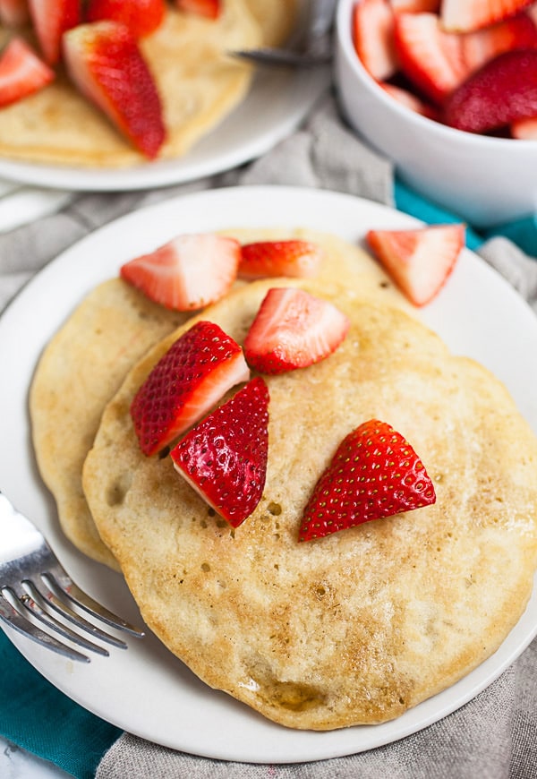 Pancakes on white plates topped with fresh chopped strawberries.