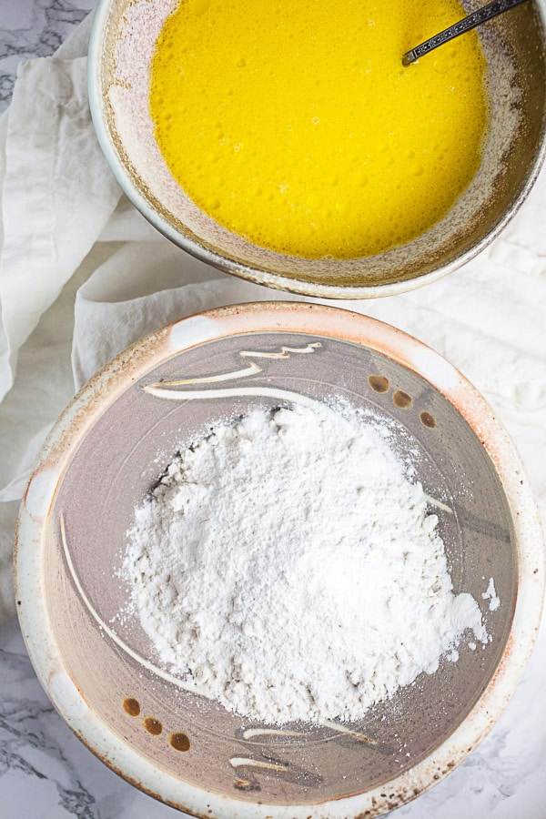 Dry and wet pancake ingredients separated into two ceramic bowls.