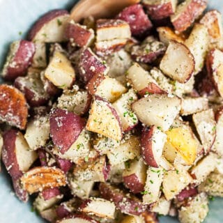 Ranch roasted red potatoes in blue serving bowl with wooden spoon.