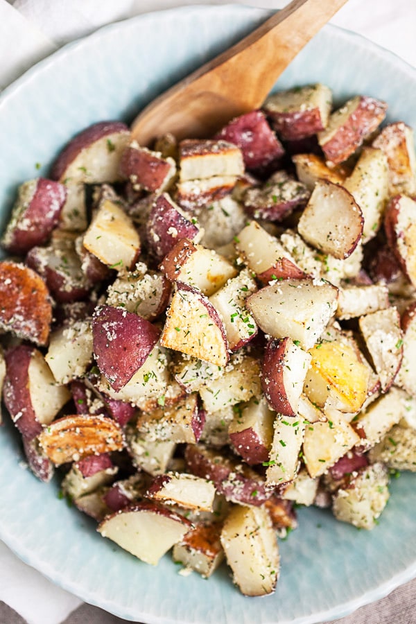 Ranch roasted red potatoes in blue serving bowl with wooden spoon.