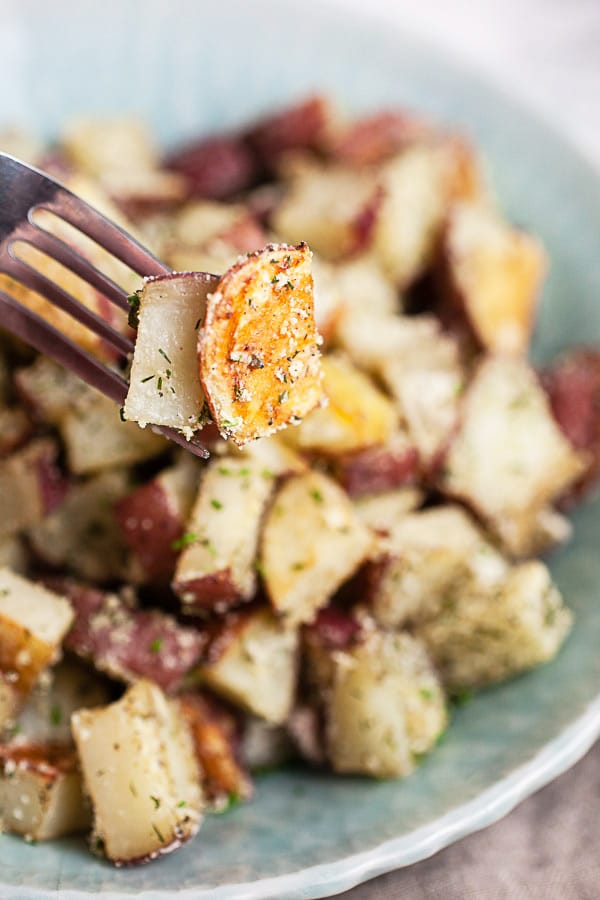 Forkful of roasted ranch potatoes lifted from blue serving bowl.