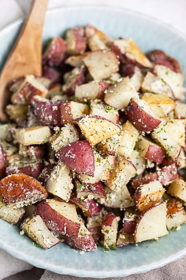 Roasted ranch seasoned red potatoes in blue serving bowl with wooden spoon.