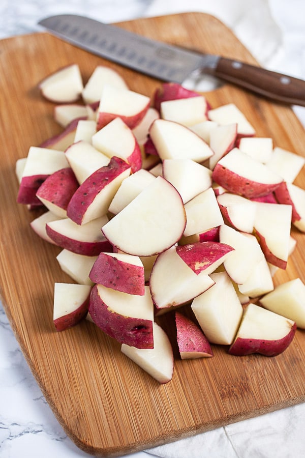 Chopped red potatoes on wooden cutting board with knife.