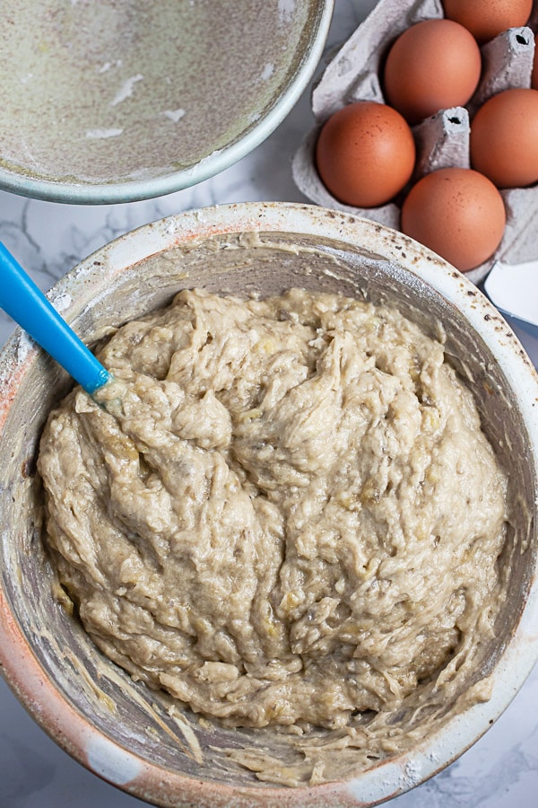 Wet and dry ingredients combined in ceramic mixing bowl next to carton of eggs.