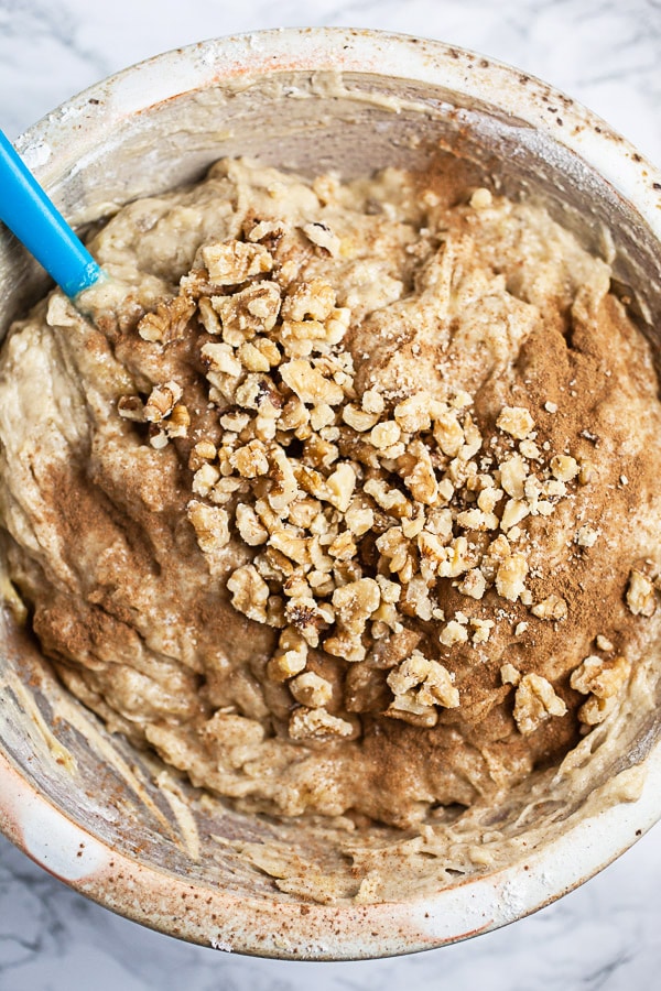 Banana bread dough with cinnamon and walnuts in ceramic bowl with blue spatula.