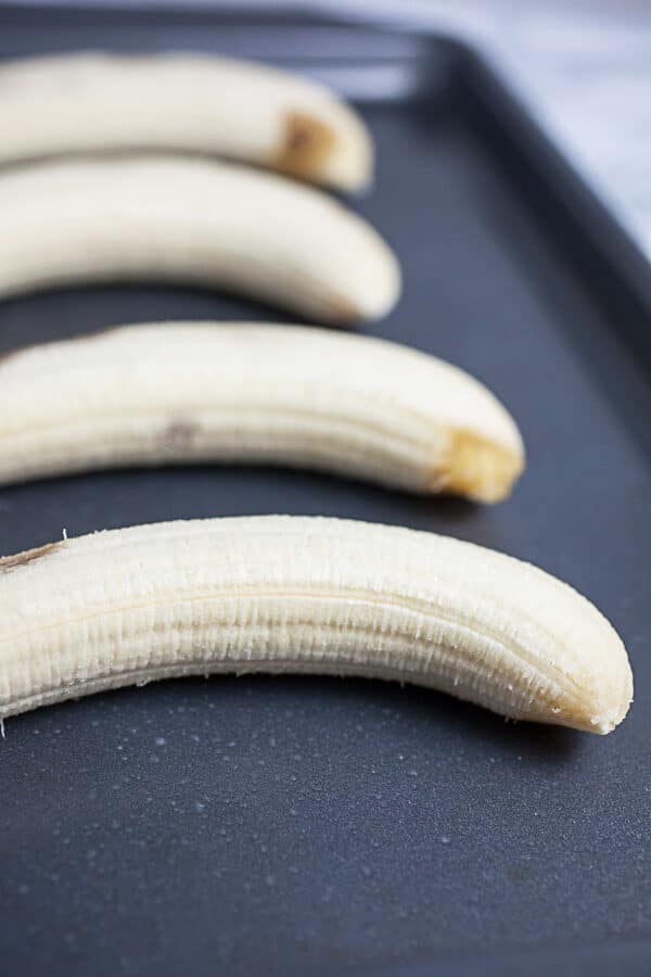 Peeled bananas lined on metal baking sheet.