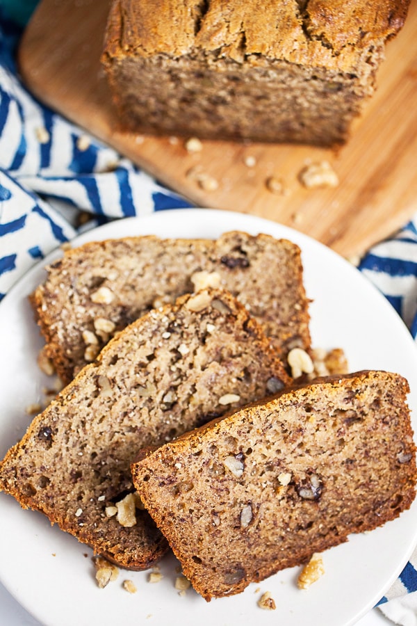 Roasted banana bread slices on small white plate next to loaf on wooden cutting board.